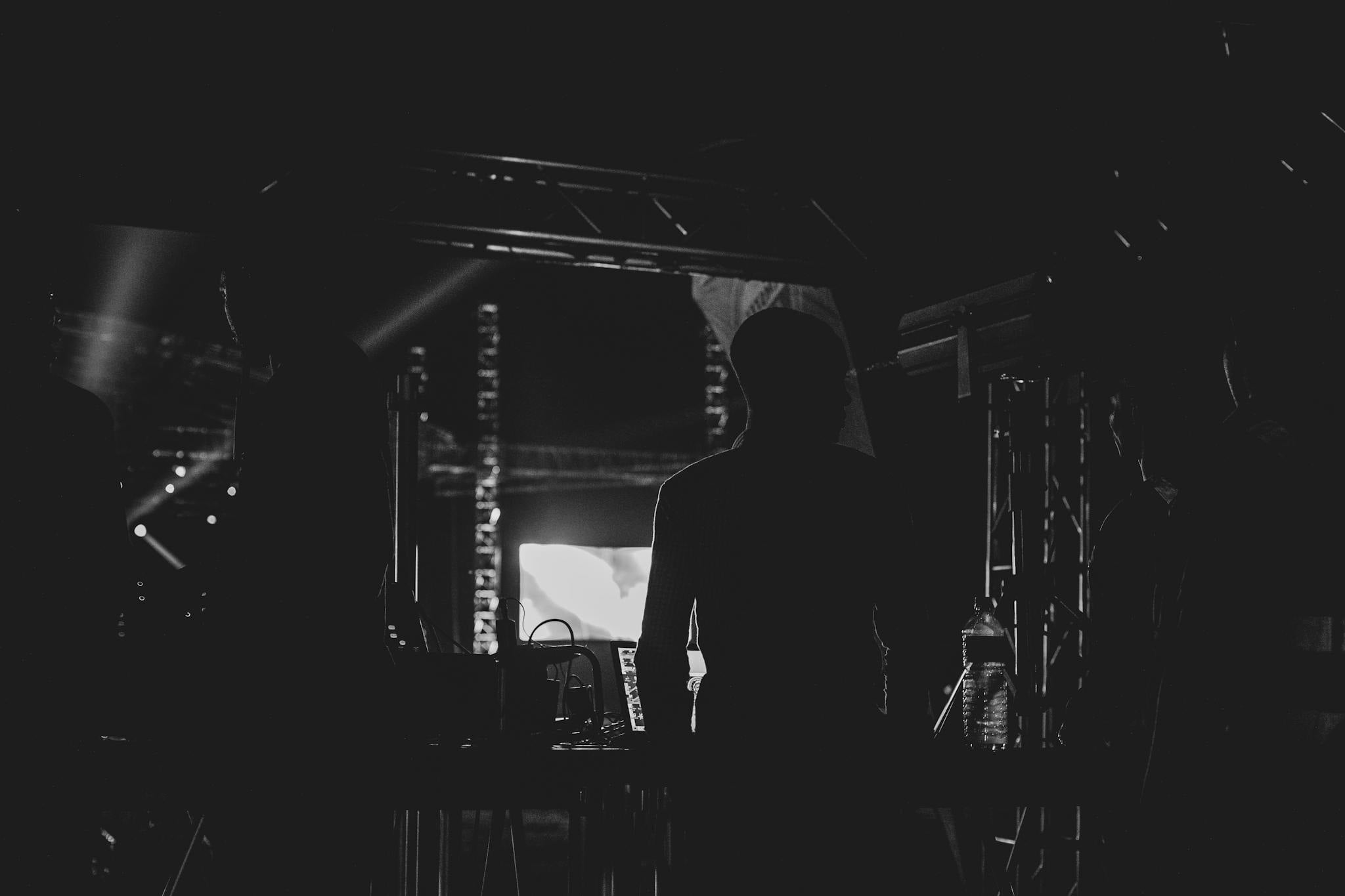 Silhouetted crew standing backstage at a concert, focusing on silhouette effect.