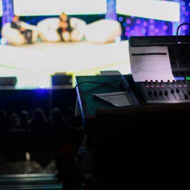 Sound console in a studio setting for a live event with blurred audience view.